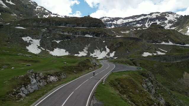 Aerial drone shot of female cyclist pushing pedals on bicycle up an asphalt road in mountains with amazing view. Cycling on a serpentine road.  Sport motivation. Active sport. 