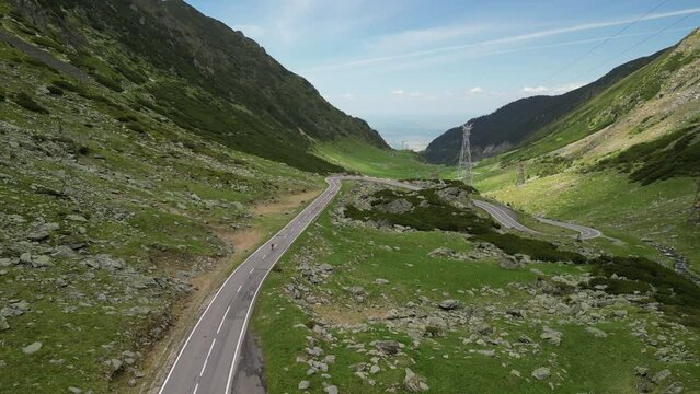 An aerial drone shot captures a female cyclist riding a bicycle on an asphalt road in the mountains, offering an amazing view. Cycling on the serpentine Transfagarasan road. Sport motivation.