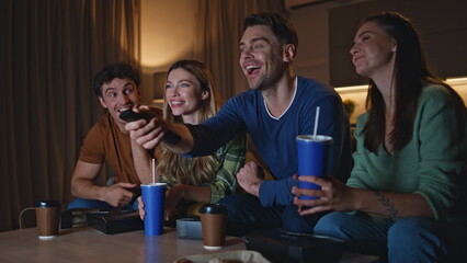 Smiling mates looking tv on couch at weekend evening. Friends watching movie