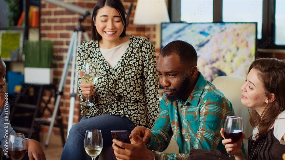 Wall mural multiracial friends at apartment party looking at funny videos on cellphone screen, sharing their im