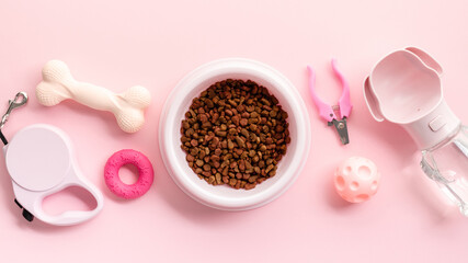 Pet supplies top view. Flat lay dry dog food in bowl, playful chew toys, a convenient leash, a practical water dispenser, essential grooming tools, and an engaging play ball on pastel pink background