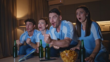 Emotional mates cheering football match at night home close up. Fans watching tv