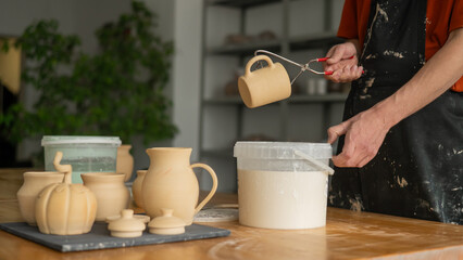 Close-up of a potter's hands glazing a ceramic mug. 
