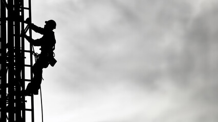 Silhouette of a construction worker at top structure wearing a hard hat in black and white with high contrast against a sky background