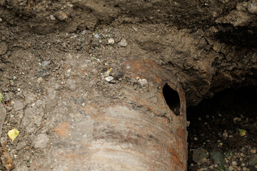 Rusty pipe is sitting in the dirt. The pipe is old and has a hole in it