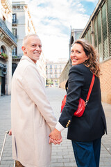 Back view of a middle aged married couple holding hands while smiling and looking at camera. Mature husband and wife having a good time on a romantic trip in Europe. Happy mid adult mates enjoying