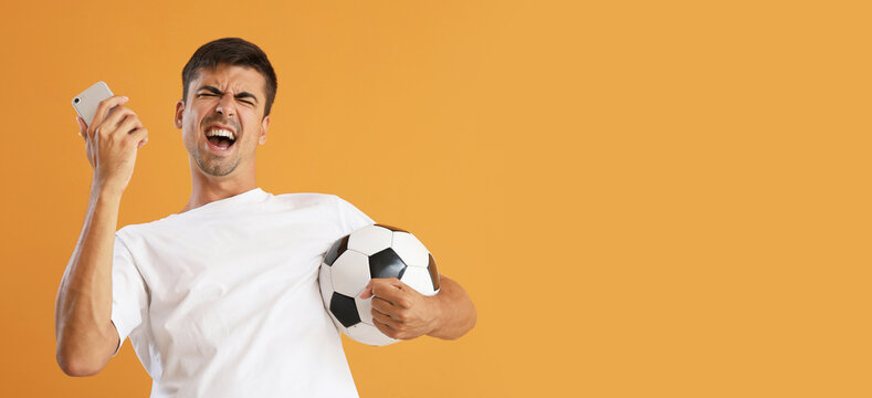 Happy man with cellphone and ball after winning of his sports bet on color background