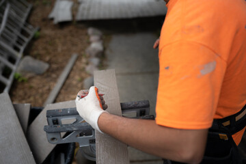 Worker in an orange shirt measuring and cutting a piece of wood for a construction project.
