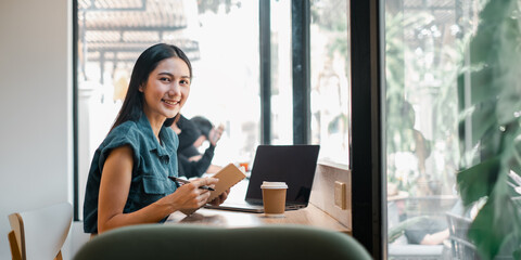 A woman is sitting at a table with a laptop and a book. She is smiling and she is enjoying her time
