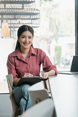 A woman is sitting at a table with a clipboard and pen. She is smiling and she is happy