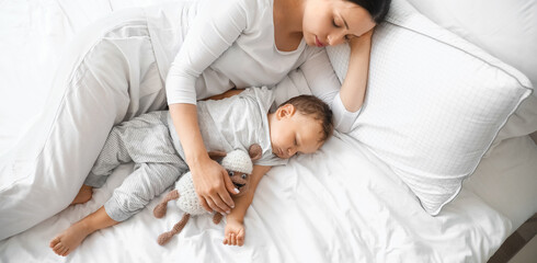 Young mother and her adorable baby with toy sleeping on bed