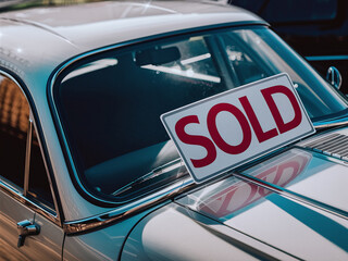 Close-up of classic car with 'SOLD' sign on windshield, indicating purchase.
