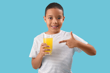Little African-American boy pointing at glass of orange juice on blue background