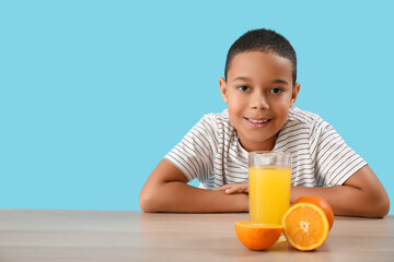 Little African-American boy with glass of orange juice at table on blue background