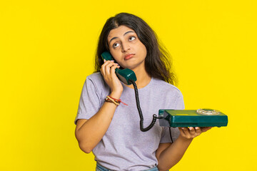 Tired bored Indian woman talking on wired vintage telephone of 80s, fooling, making silly faces,...