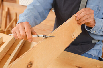 Mature carpenter working with wooden plank at table in shop, closeup