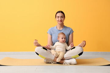 Beautiful young sporty woman with her little baby meditating near yellow wall