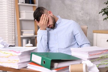 Obraz premium Overwhelmed man surrounded by documents at workplace in office