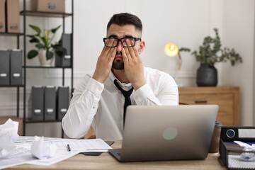 Naklejka premium Overwhelmed man sitting at table with laptop and documents in office
