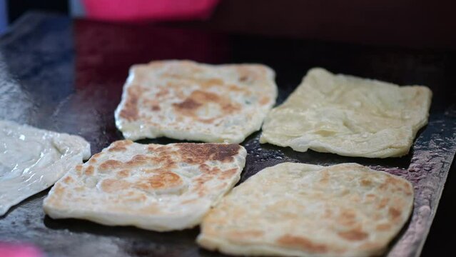 Street food vendor is preparing the dough and pan-frying paratha roti in hot oil until crispy on the outside. Street hawker preparing prata bread or roti canai for morning breakfast