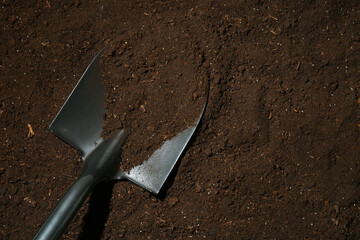 Metal shovel on fertile soil, top view and space for text. Gardening tool