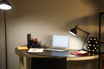 Blurred view of office with workplace and glowing lamps at night