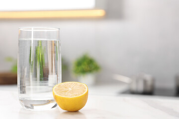 Glass with clear water and half of lemon on white table in kitchen, space for text