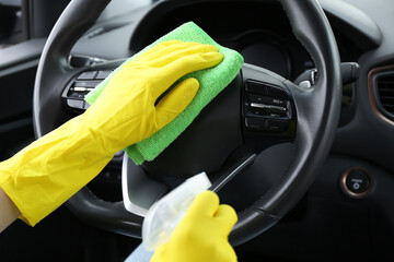Woman cleaning steering wheel with rag in car, closeup