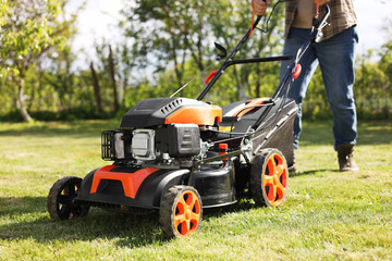 Man cutting green grass with lawn mower in garden, selective focus