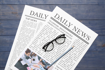 Newspapers with glasses and pencil on blue wooden background
