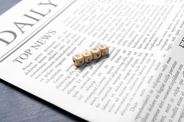 Daily newspaper and word NEWS made of cubes on blue wooden background