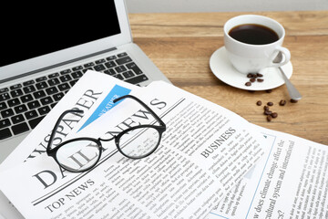 Newspapers with glasses, laptop and cup of coffee on wooden table