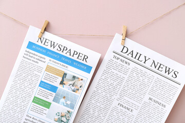 Different newspapers hanging on rope against pink background