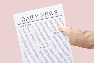 Female hand with daily newspaper on pink background