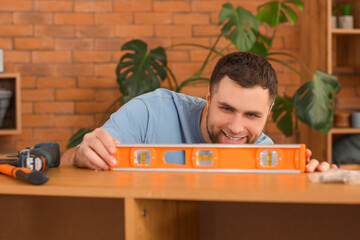 Young man with level assembling chest of drawers at home