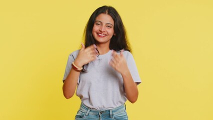 Young Indian woman smiling friendly at camera, waving hands gesturing hello greeting or goodbye welcoming with invitation hospitable expression. Arabian Hindu girl isolated on yellow studio background