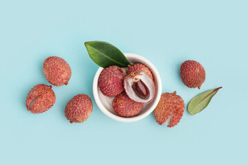 Bowl with tasty litchi fruit on blue background