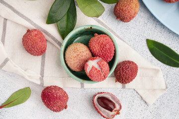 Bowl with tasty litchi fruit and leaves on light background