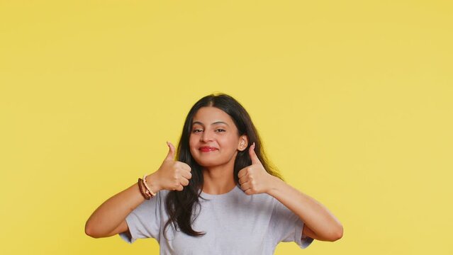 Indian woman showing thumbs up pointing overhead, above head empty place, advertising area for commercial text copy space for goods promotion advertisement. Arabian girl isolated on yellow background