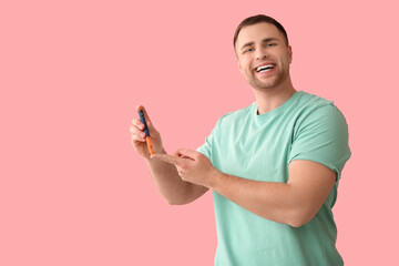 Handsome young happy diabetic man using lancet pens on pink background