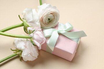 Beautiful ranunculus flowers with gift box on beige background