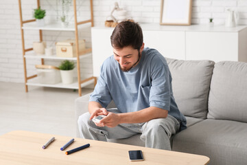 Diabetic young man using glucometer on sofa at home
