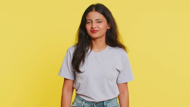 Surprised funny comical playful Indian woman making fish grimace pout lips, smooching choking and looking with shocked dumb idiotic expression doing duck face fooling around. Girl on yellow background