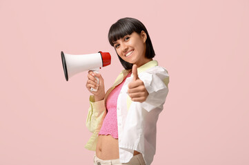 Young woman with megaphone showing thumb-up on pink background