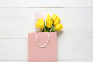 Paper shopping bag with yellow tulips on white wooden background