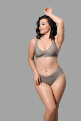 Beautiful young happy body positive woman in stylish underwear on grey background