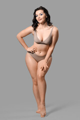 Fototapeta premium Beautiful young happy body positive woman in stylish underwear on grey background