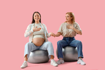 Mature doula with pregnant woman on fitballs holding hands against pink background