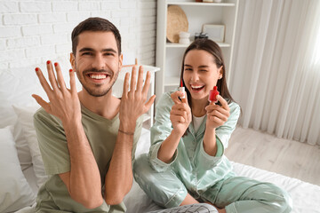 Young man with applied nail polish and his wife in bedroom