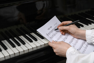 Female hands with pen and music sheets near piano